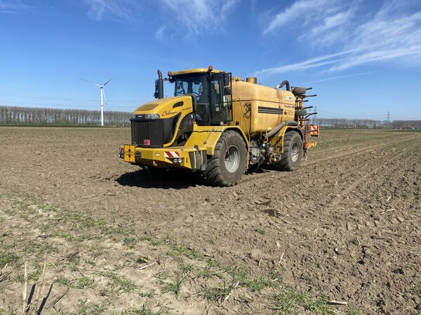 Gele Challenger TerraGator zelfrijdende bemester op een pas bewerkt perceel met windmolen