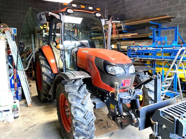 Kubota M8560 met frontlader-aanbouw in een werkplaats naast een gele veldspuit