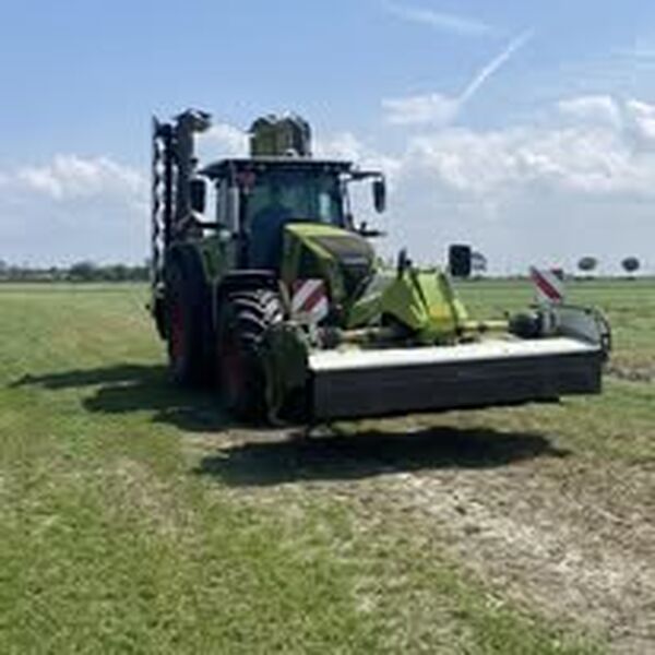 Claas-tractor met brede frontmaaier op een pas gemaaid grasland